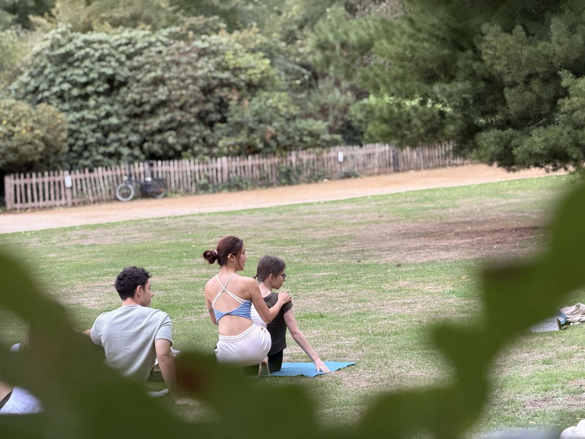 Seen through leaves, Zu kneels beside a student offering an adjustment
