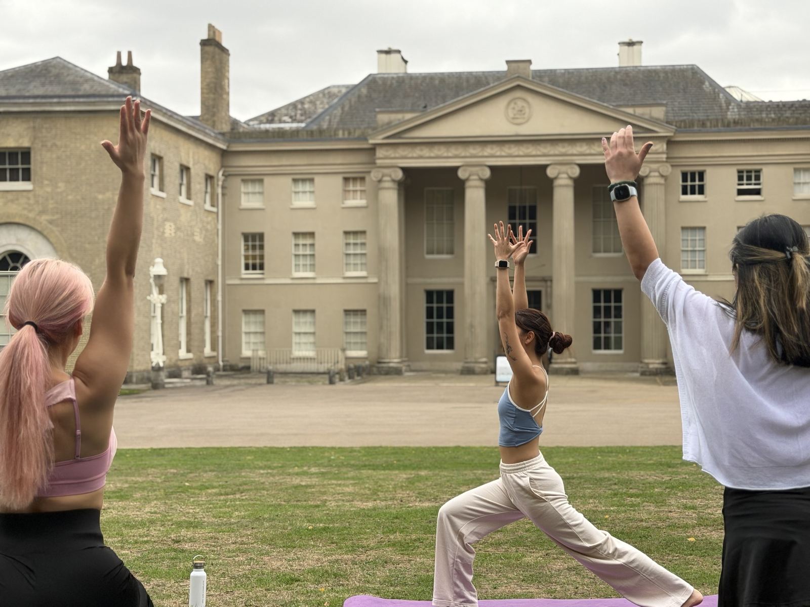 Zu in warrior one in front of a columned Georgian house, students raising their arms