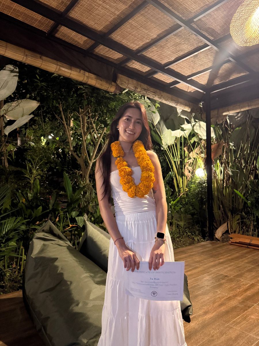 Zu wearing a marigold garland, holding her yoga teacher training certificate in Bali