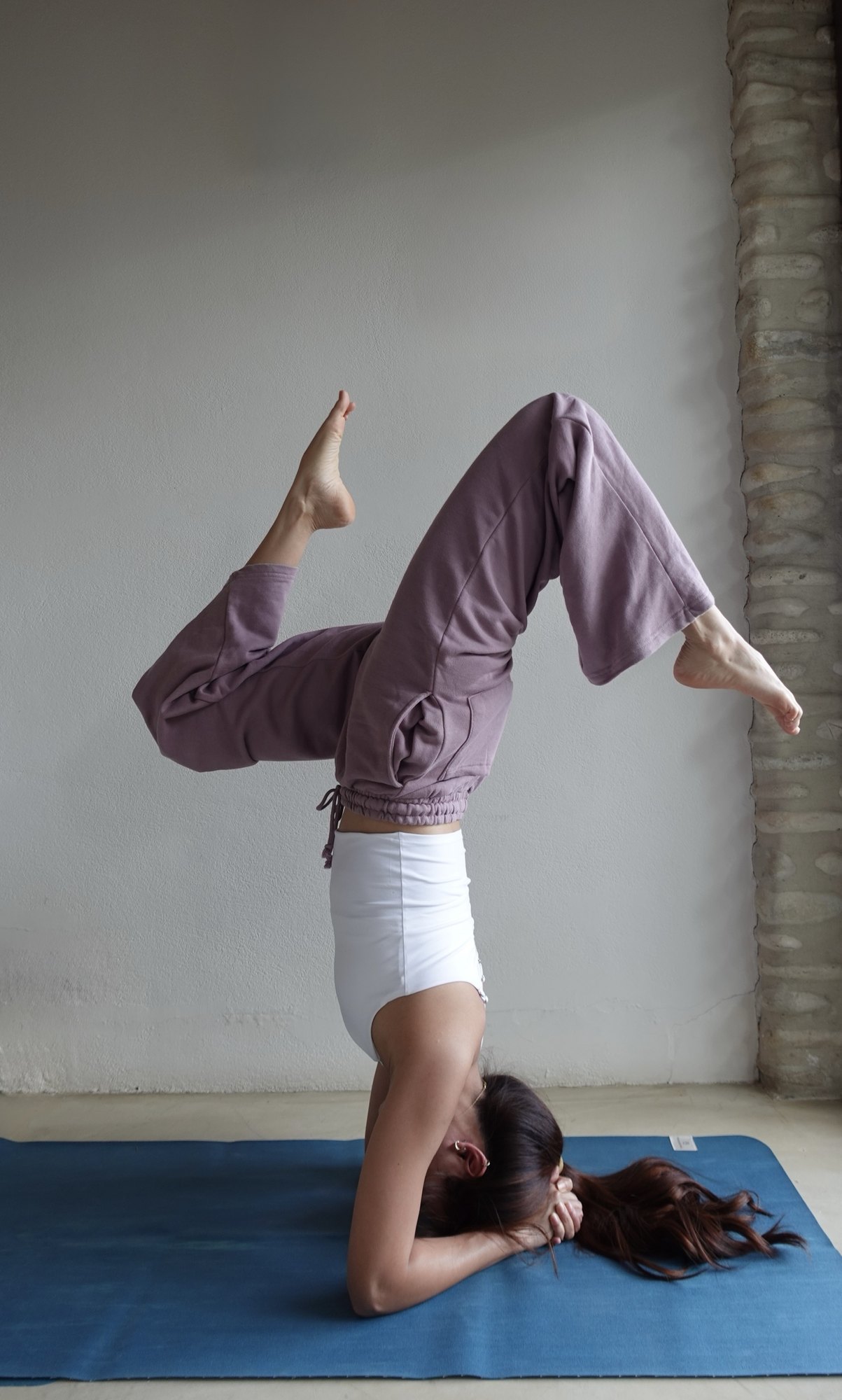 Zu holding a headstand with bent knees beside a white wall