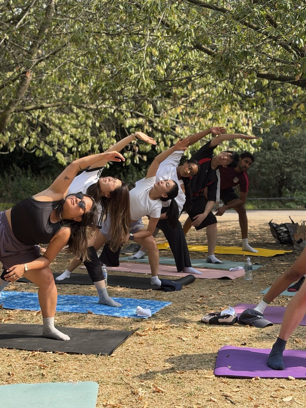 A park yoga class reaching into an extended side angle stretch under the trees