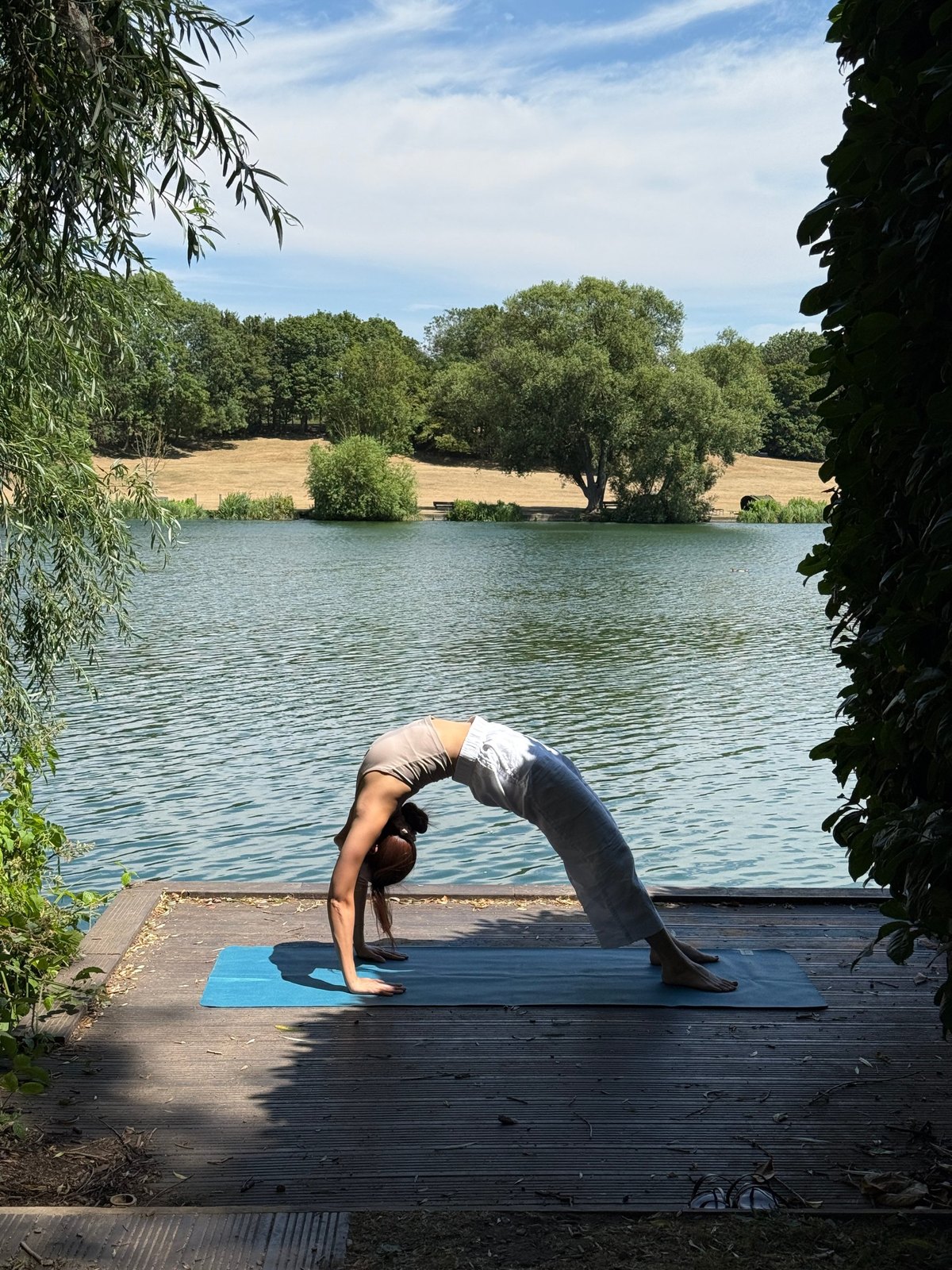 Zu in wheel pose on a wooden jetty by a lake, framed by willow trees
